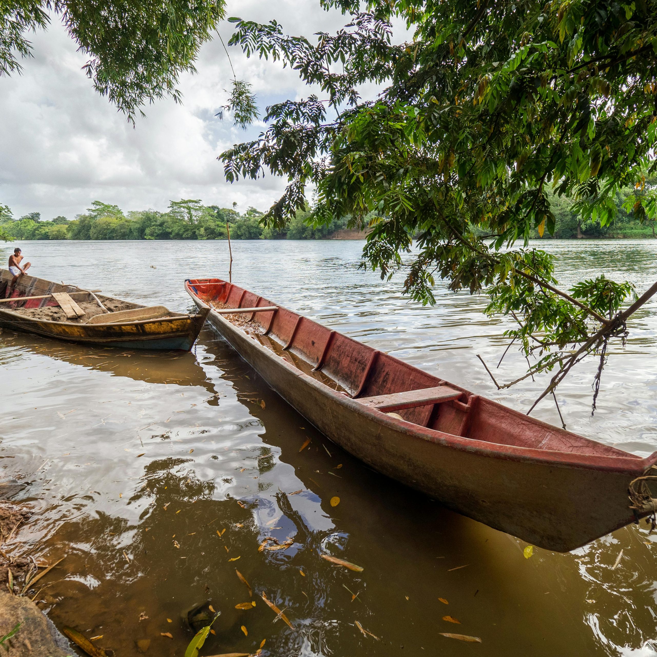 Wooden fishing boats resting by the lush banks of Rio Rama, Nicaragua, under a cloudy sky.
