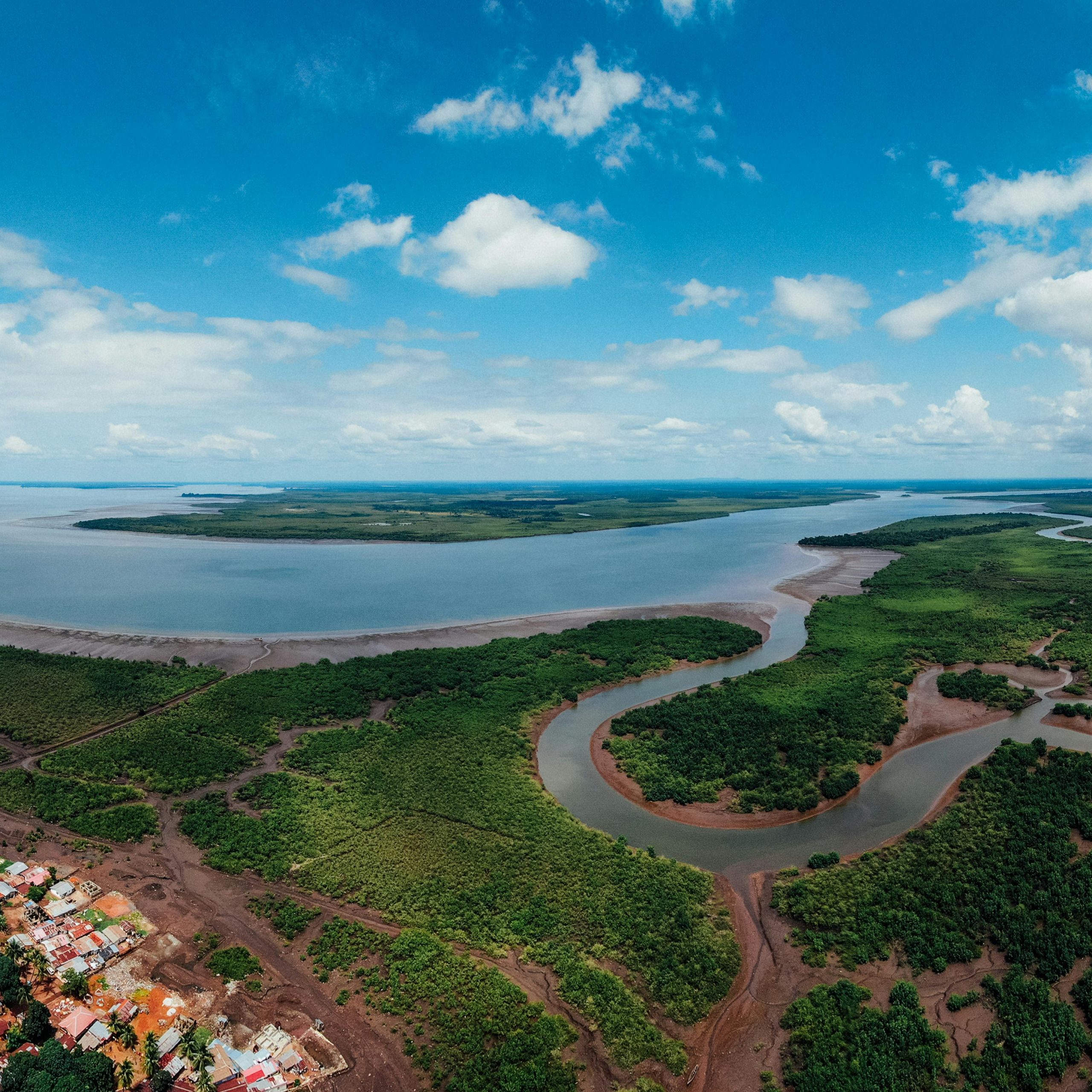 Panoramic aerial view of a coastal city with lush greenery, winding river, and expansive blue sky.